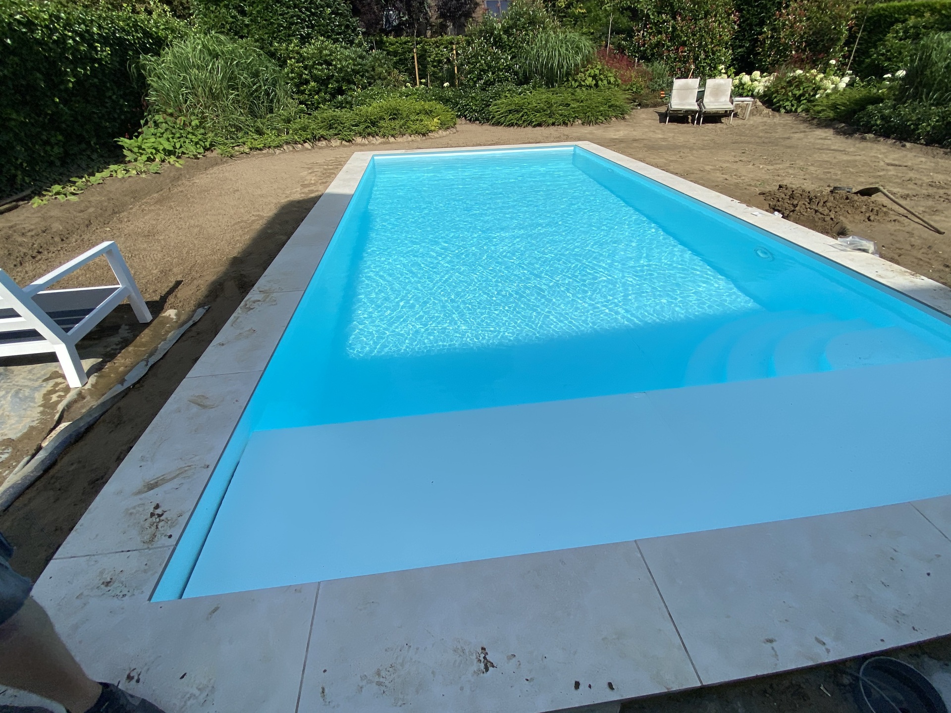 Rechthoekig zwembad met turkoois water, lichte natuurstenen boord en tuin in aanleg door Liner Plaatsen